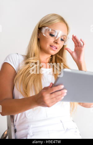 A beautiful young blond woman siting on a ladder and using a tablet Stock Photo
