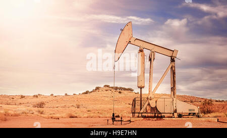 Retro toned panoramic picture of an oil pump, old industrial equipment on arid soil. Stock Photo