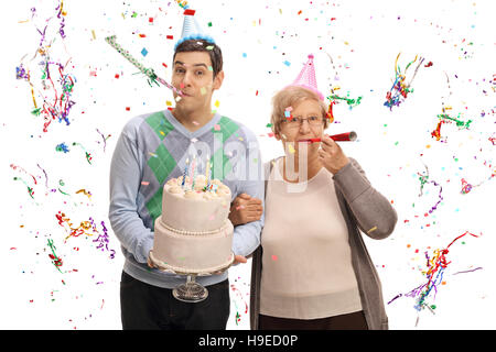 Young man with a birthday cake and a mature woman blowing party horns isolated on white background Stock Photo