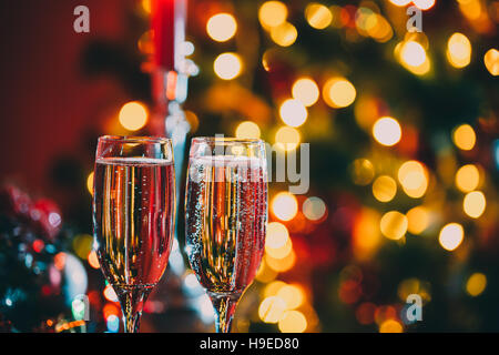 Beautiful two glasses of champagne standing on the table in the background of a blurred room with a decorated Christmas tree and fireplace. Soft focus Stock Photo