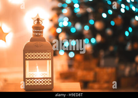 Close-up of Christmas lantern with burning candles on blurred background living room with Christmas tree. Stock Photo