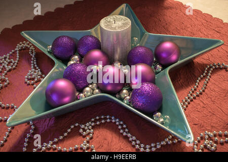 A silver candle in a star-shaped Dekoschale with purple Christmas balls, on a red tablecloth decorated with a silver Pearl Necklace Stock Photo