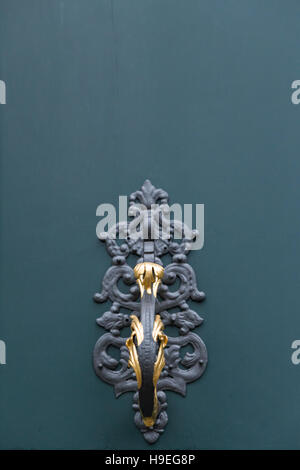 A dark green painted wooden door of a villa with elegant metal ornaments, golden knobs and knocker. Detail view of a knocker. Stock Photo