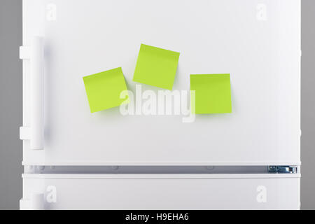Three blank green sticky paper notes on white refrigerator door Stock Photo