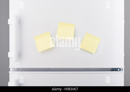 Three blank light yellow sticky paper notes on white refrigerator door Stock Photo