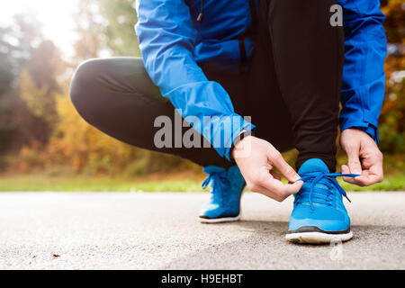 Unrecognizable runner crouching, tying shoelaces, close up Stock Photo