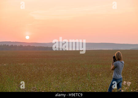Caucasian woman photographing sunset in field Stock Photo
