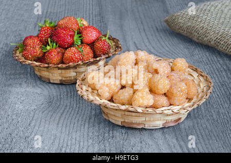 Raspberries and strawberries in wicker baskets, on wooden surface Stock Photo