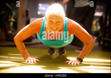 Smiling older woman doing push-up on gymnasium floor Stock Photo