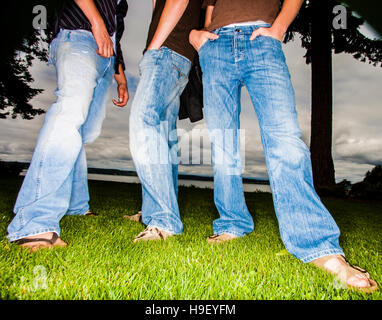 Legs of friends wearing jeans in grass Stock Photo