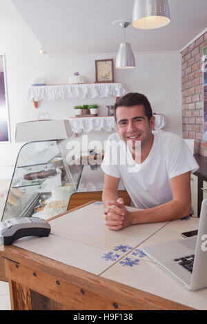 Smiling Hispanic baker leaning on counter Stock Photo
