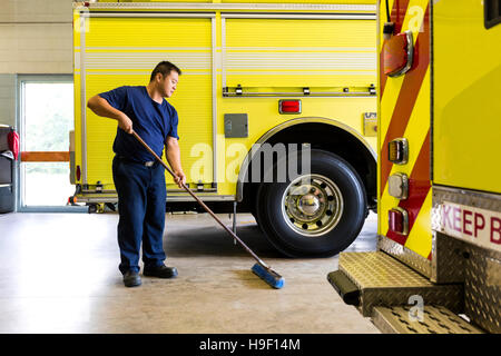 Chinese fireman sweeping floor near fire trucks Stock Photo