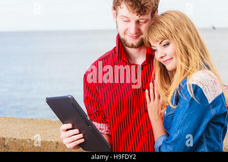 Modern technology devices and tourism concept. Young couple outdoor against sea water with tablet enjoying summer holidays Stock Photo