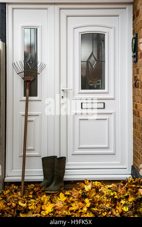 Boots and rake with pile of leaves by front door. Stock Photo