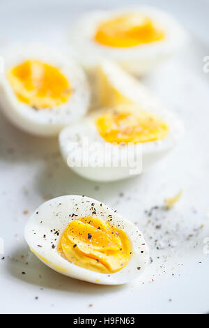 hard boiled organic free range eggs cut in half sprinkled with salt and pepper against a white backdrop with a shallow DoF Stock Photo