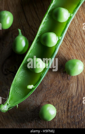 Close up of bright green summer peas in a pea pod on wooden backdrop open to show fresh peas. Additional peas lying on counter. Stock Photo