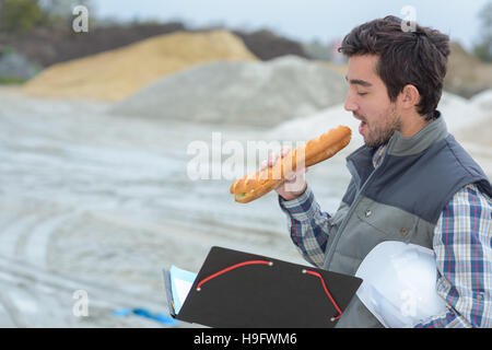 Man eating baguette on building site Stock Photo