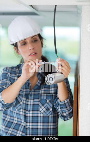female technician installing camera on wall with screwdriver Stock Photo