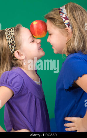 Two girls holding an apple between the foreheads Stock Photo