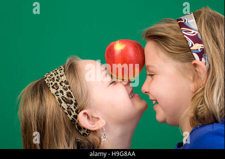 Two girls holding an apple between the foreheads Stock Photo