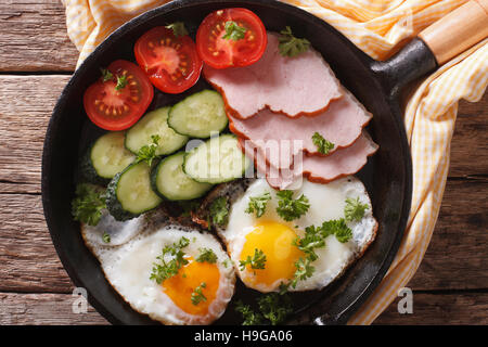 fried eggs with ham, tomatoes and cucumbers in a pan close-up. horizontal view from above Stock Photo