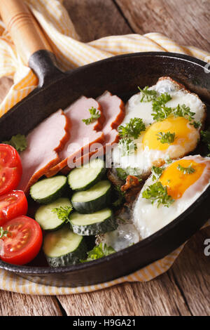 fried eggs with ham, tomatoes and cucumbers in a pan close-up. vertical Stock Photo