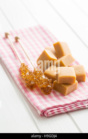Brown sugar crystals on stick and caramel candies on checkered napkin. Stock Photo