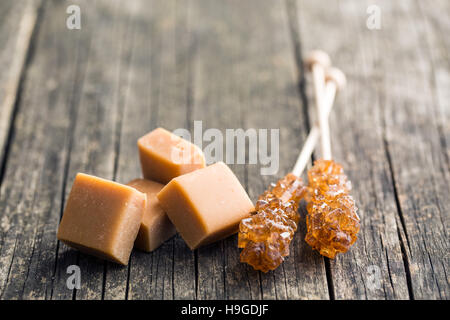 Brown sugar crystals on stick and caramel candies on old wooden table. Stock Photo