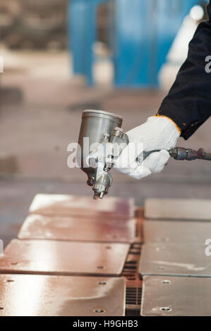 Hand with cotton glove holding a spray painting gun at an industrial paint shop. Stock Photo