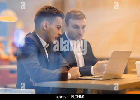 Two young co-workers looking at financial statistics on laptop display Stock Photo
