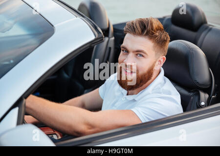 Happy young man driving cabriolet and looking at camera Stock Photo