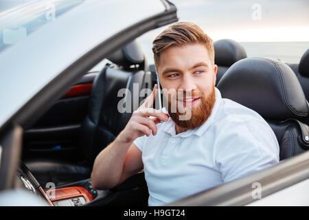 Young bearded man talking on his phone and driving a cabriolet car Stock Photo