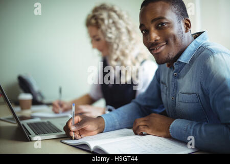 Business executive taking notes while using laptop Stock Photo