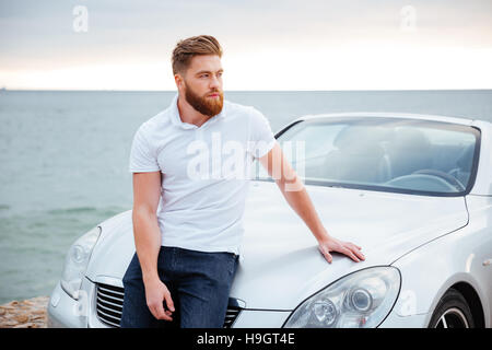 Young bearded man leaning on his car parked on beach Stock Photo