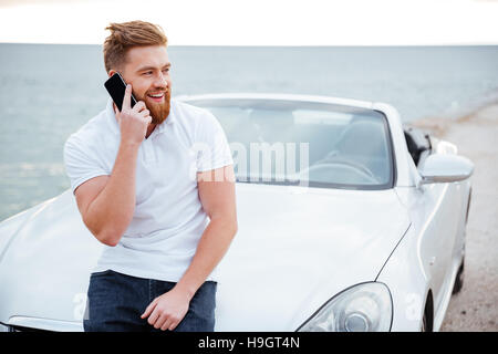 Handsome young man talking on the mobile phone while leaning at his car Stock Photo