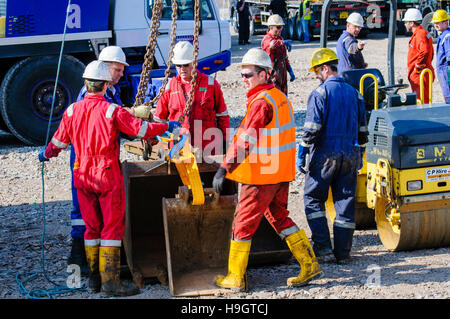Construction workers prepare a crane hook to lift backhoe digger buckets.at an exploratory oil well. Stock Photo