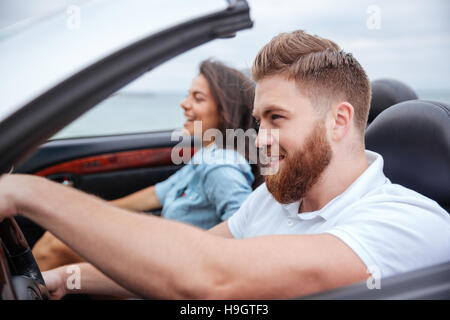 Happy young couple smiling while sitting inside of their convertible Stock Photo