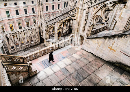 A nun walks towards one of the massive flying buttress and ornately carved stonework on the roof of the Duomo Milano, Italy Stock Photo