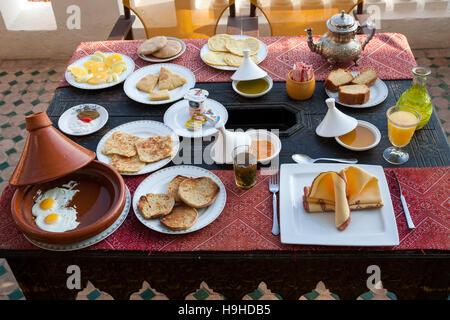 A richly laid Moroccan breakfast with fried eggs in a tagine, several kinds of bread, honey, yoghurt and freshly squeezed orange juice is set out on the rooftop terrace of the Riad Arabesque in Fès, Morocco. Stock Photo