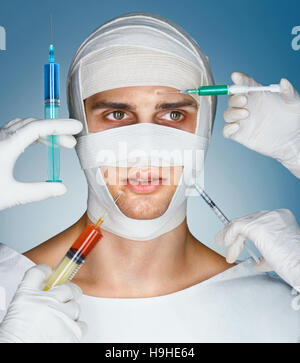 Man's face wrapped in bandages while many hands holding syringes near his face. Plastic surgeons giving injection. Beauty concept Stock Photo