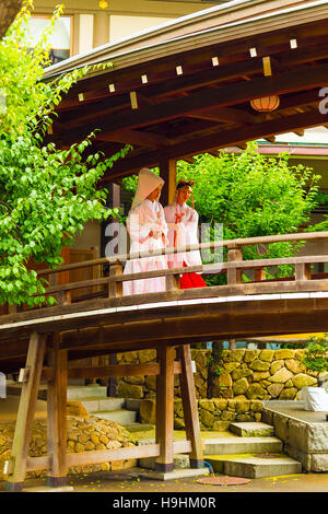 A miko maiden guides a bride in white traditional kimono during a Shinto wedding across wooden bridge at Yushima Tenmangu shrine Stock Photo