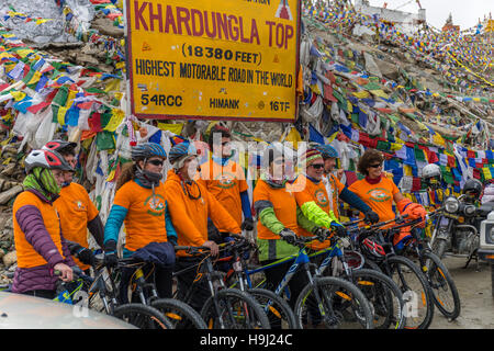 Group of cyclists pose in front of a wall of prayer flags at the top of Khardungla Pass Stock Photo