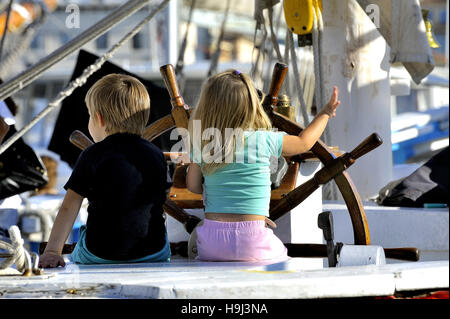 Two young children on the stand of an old wooden sailing ship cruising imagining in full Stock Photo