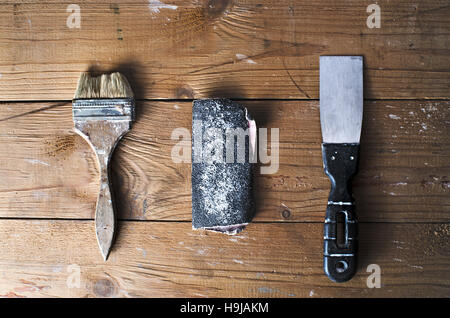 Old brush, sandpaper and trowel on a brown tattered wooden background, top view, joinery work, home repairs Stock Photo