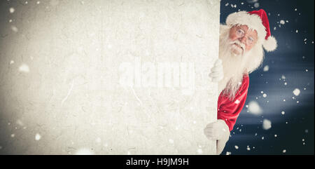 Composite image of santa looks out behind a wall Stock Photo