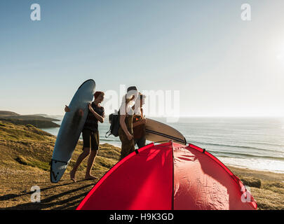 Three friends with surfboards camping at seaside Stock Photo