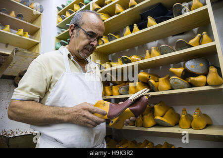 Shoemaker selecting shoe lasts from a shelf in his workshop Stock Photo