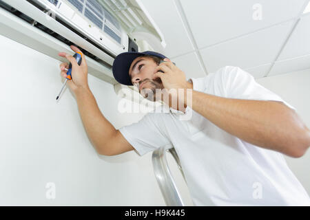young handyman repairing air conditioning system calling for help Stock Photo