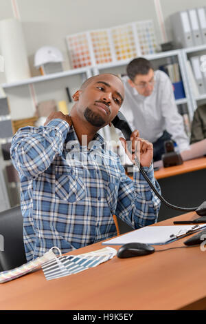 Man sat at desk, on telephone, stretching neck Stock Photo