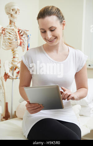 Female Osteopath In Consulting Room Using Digital Tablet Stock Photo